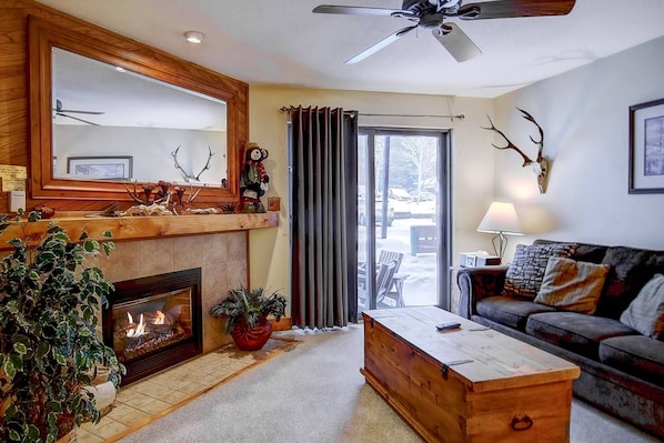 Un salon chaleureux avec une cheminée, une table basse en bois, un canapé, un grand miroir et un ventilateur de plafond.