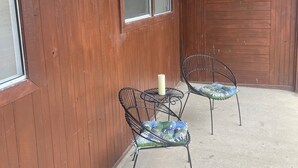 A wooden exterior wall with a window and two metal chairs with cushions.
