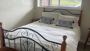 A single bed with a wooden headboard and footboard, a bench, and a window with a view of greenery.