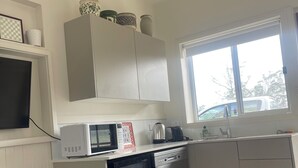 A compact kitchen with a microwave, toaster, and dishwasher. A window provides natural light, and a small trash bin is visible.