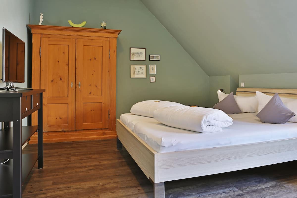 A bedroom with a bed, a wooden wardrobe, a desk, and a nightstand.