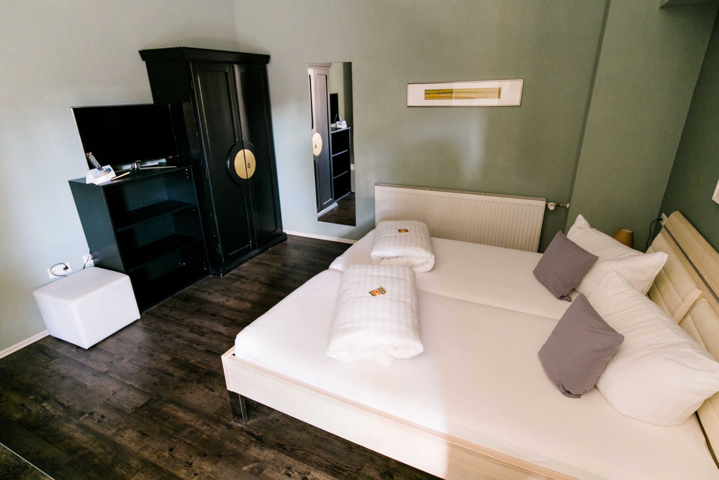 A bedroom with a large bed, a wardrobe, a television, and a mirror.