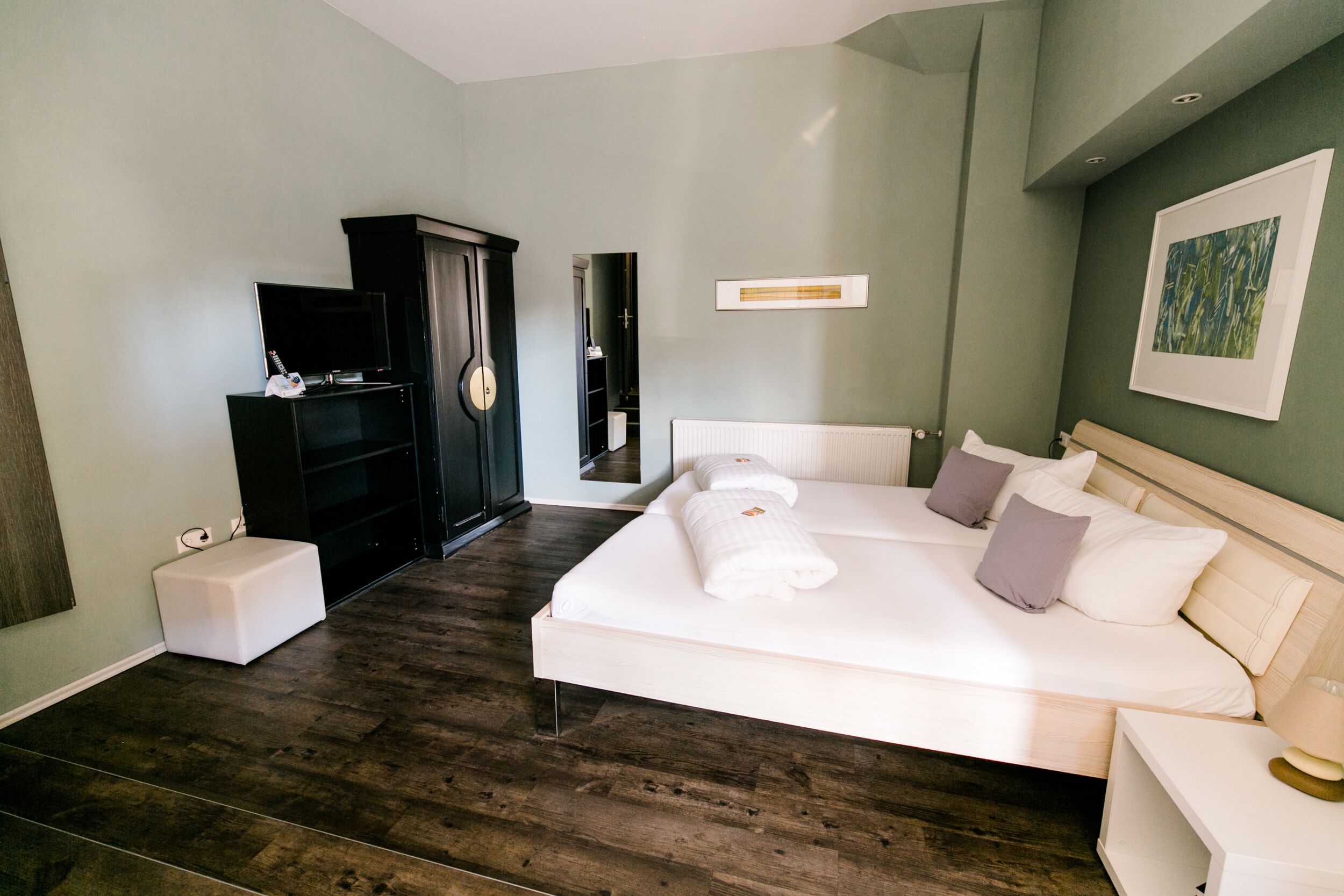 A modern hotel room with a large bed, a TV, a wardrobe, and a mirror.