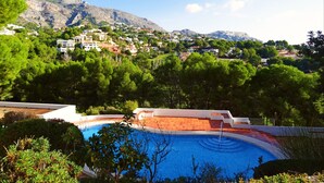 Une piscine entourée d’une végétation luxuriante et un village perché sur une colline.