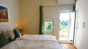 Une chambre à coucher comprenant un lit, une table de chevet, une lampe, une fenêtre avec des rideaux et un appareil de climatisation.