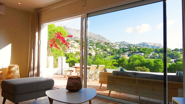 Un salon moderne doté d’une grande porte-fenêtre coulissante donnant sur un balcon avec vue sur une ville située sur une colline.