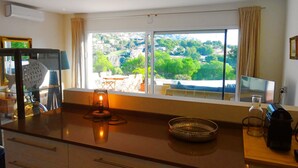 Une cuisine moderne dotée d’une grande fenêtre, un coin repas avec du mobilier d’extérieur et une vue sur un paysage verdoyant.