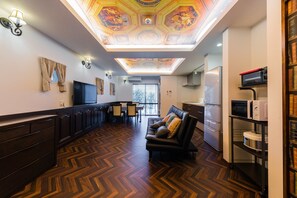 Relax in a spacious room with a high ceiling, featuring a unique hexagonal patterned design. Enjoy a seating area with a sofa and dining table, plus a kitchenette with a refrigerator and microwave.