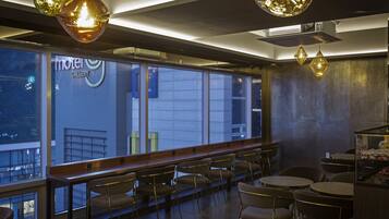 Un restaurante moderno con vistas a la ciudad, que cuenta con una barra larga con sillas, iluminación colgante y un letrero visible que dice 'Motel Gallery'.