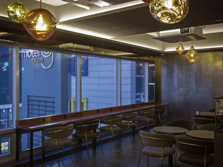 Un restaurante moderno con vistas a la ciudad, que cuenta con una barra larga con sillas, iluminación colgante y un letrero visible que dice 'Motel Gallery'.
