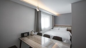 Habitación de hotel moderna con cama, escritorio y silla. Cuenta con una ventana con cortinas, una lámpara en el techo y un panel de control en la pared.