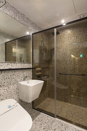 Un baño moderno con un lavamanos blanco, una cabina de ducha con mampara de vidrio y un espejo grande.