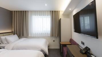 A hotel room with two beds, a TV, a desk, and a window with curtains.