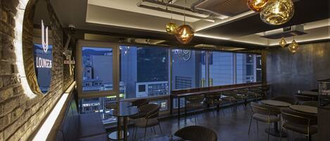 A modern lounge area with seating, a large window offering a city view, and a sign indicating the lounge's name.