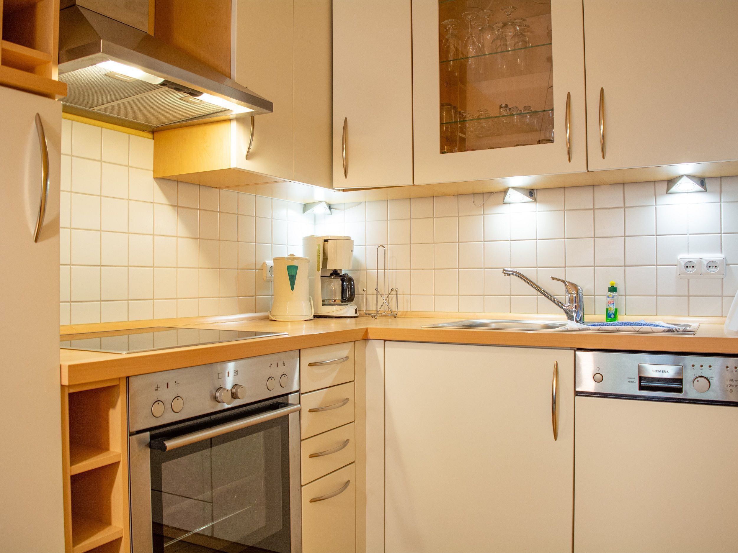 A modern kitchen with white cabinets, a built-in oven, a coffee maker, and a sink with a faucet.