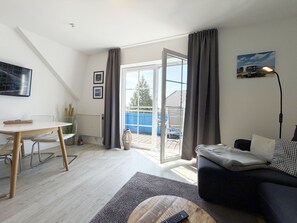 En moderne stue med sofa, sofabord, spisebord med stole, radiator, stort vindue med gardiner og et billede på væggen.