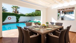 Un coin repas avec vue sur la piscine, des meubles en osier et une table dressée pour quatre personnes.