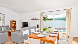 Un salon moderne comprenant un coin repas, un ensemble de canapés, un téléviseur et un balcon avec vue sur la mer.