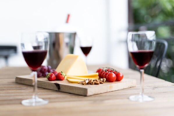 Ett träbord med en ostbricka, vindruvor, tomater och två glas rött vin.