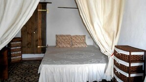 A bedroom with a bed, curtains, a wooden wardrobe, and a patterned rug. - DOMUSANTIGA - Love nest (studio flat) a few minutes from the sea (San Giovanni Suergiu)