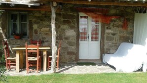 A stone building with a wooden table and chairs outside, a white door with curtains, and a covered porch area. - DOMUSANTIGA - Love nest (studio flat) a few minutes from the sea (San Giovanni Suergiu)