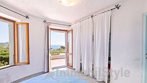 Et soveværelse med en stor seng, en skydedør til en balkon og udsigt over landskabet.
