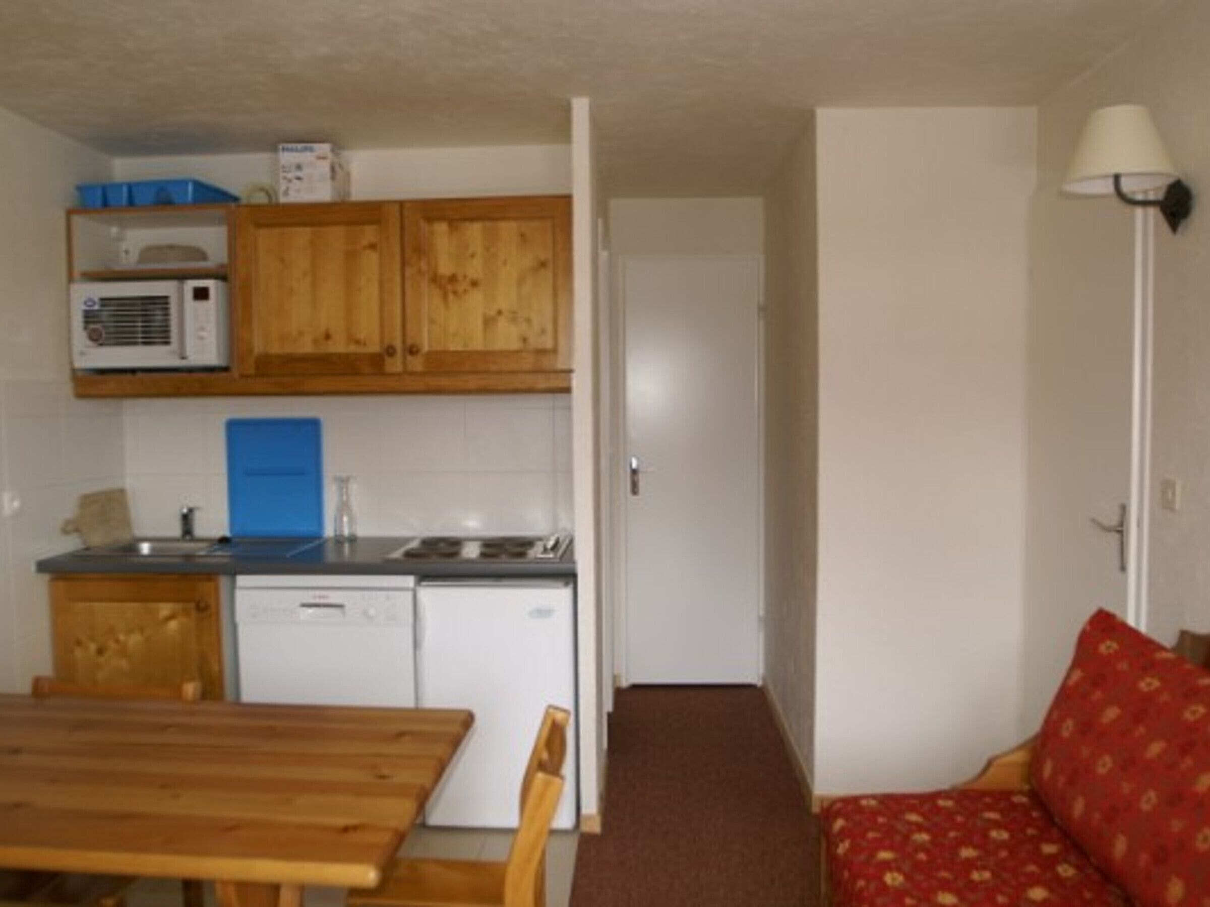 A compact kitchen with wooden cabinets, a microwave, a sink, and a dishwasher.