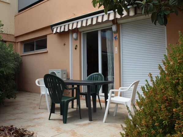 Une terrasse extérieure avec une table et des chaises, une porte-fenêtre coulissante et un auvent blanc.