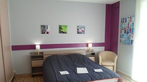 Un dormitorio con cama, mesitas de noche, una silla y decoración en la pared.
