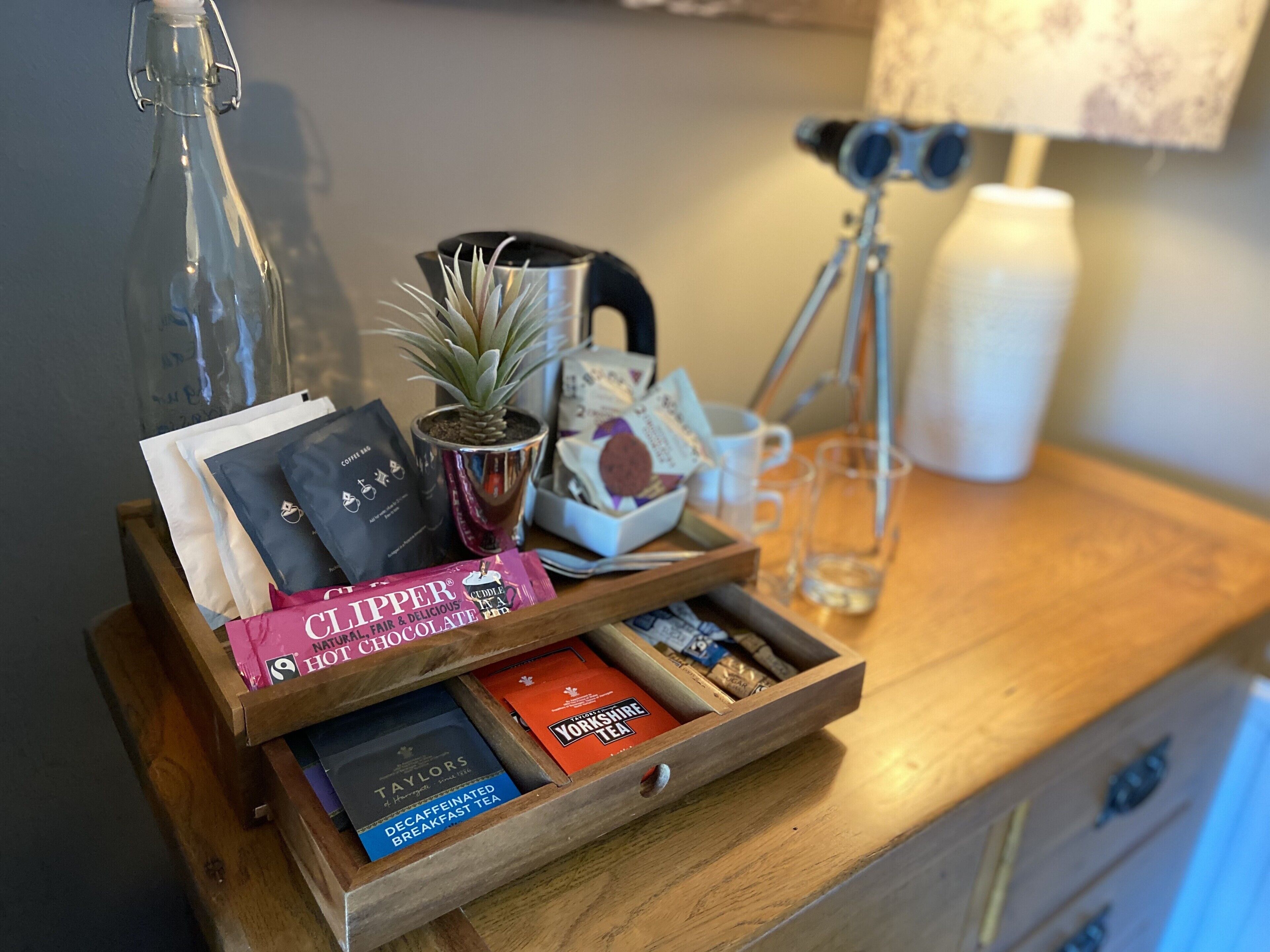 Un plateau en bois avec des sachets de thé, une plante en pot et une machine à café, le tout posé sur une table en bois.