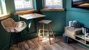 A room with a wooden desk, two chairs, a small stool, a television, and a window with a view of the outside. - The Riverside Rooms (Newark)