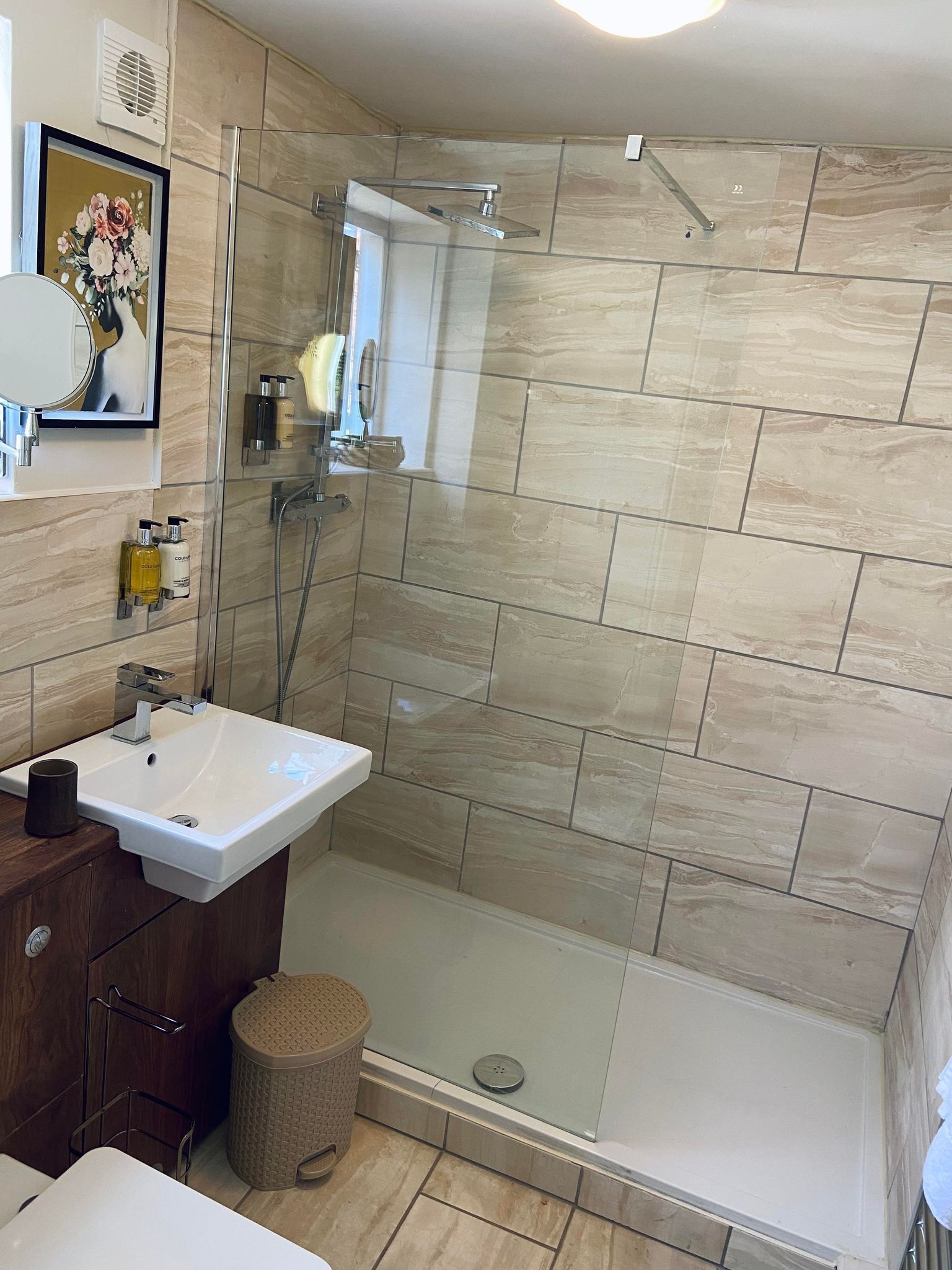 A modern bathroom with a glass-enclosed shower, a white sink, and a wooden vanity.