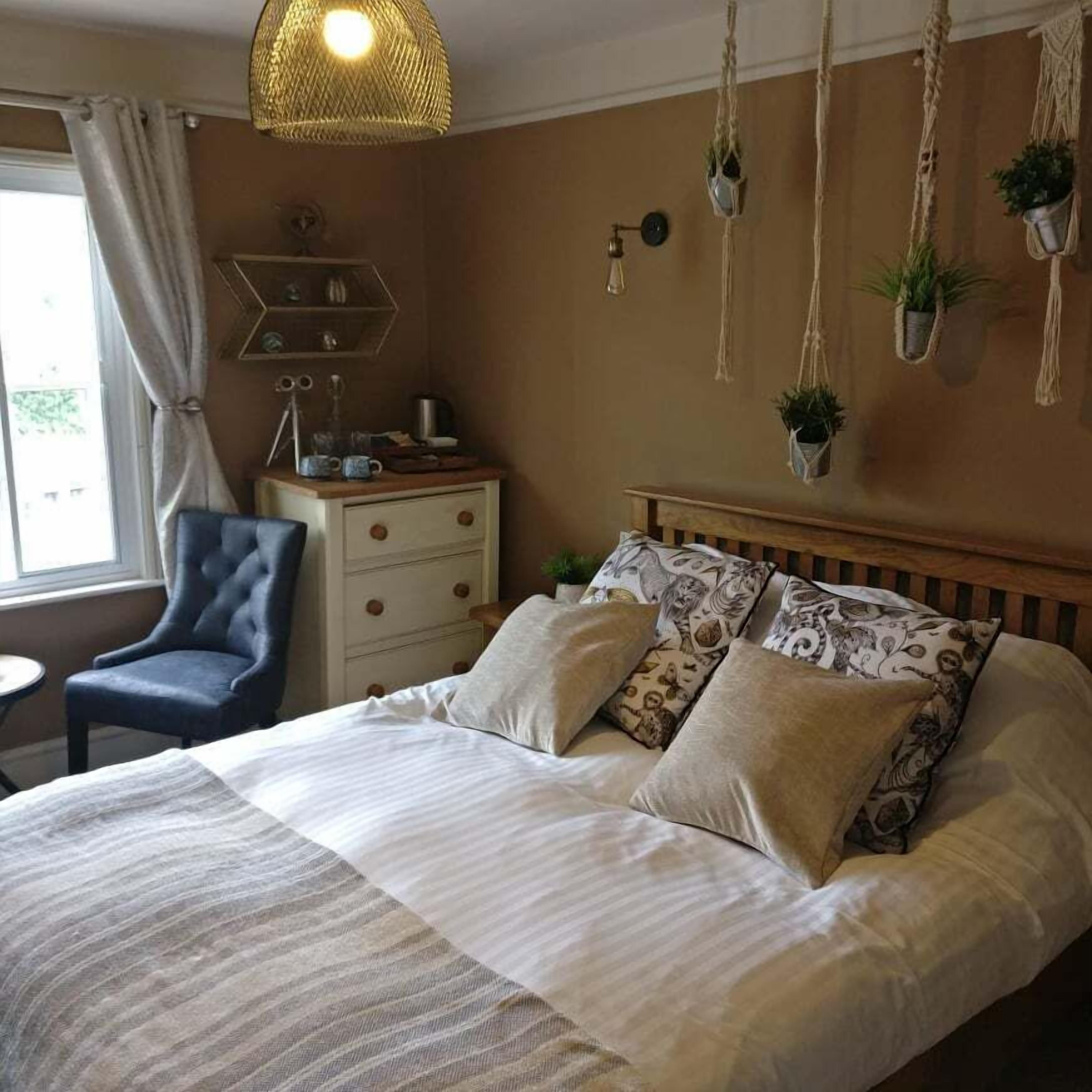 Un dormitorio con cama, una silla, cómoda y adornos de macramé en las paredes.