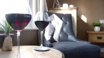 A room with a round wooden table, two wine glasses, a potted plant, and a grey upholstered chair.