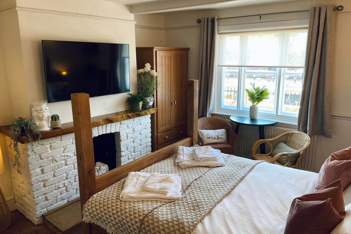 A hotel room with a fireplace, a television, a bed with a quilt, a chair, and a window with curtains.