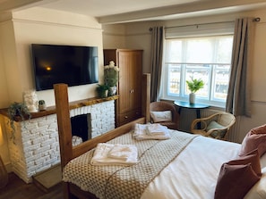 A hotel room with a fireplace, a television, a bed with a quilt, a chair, and a window with curtains.