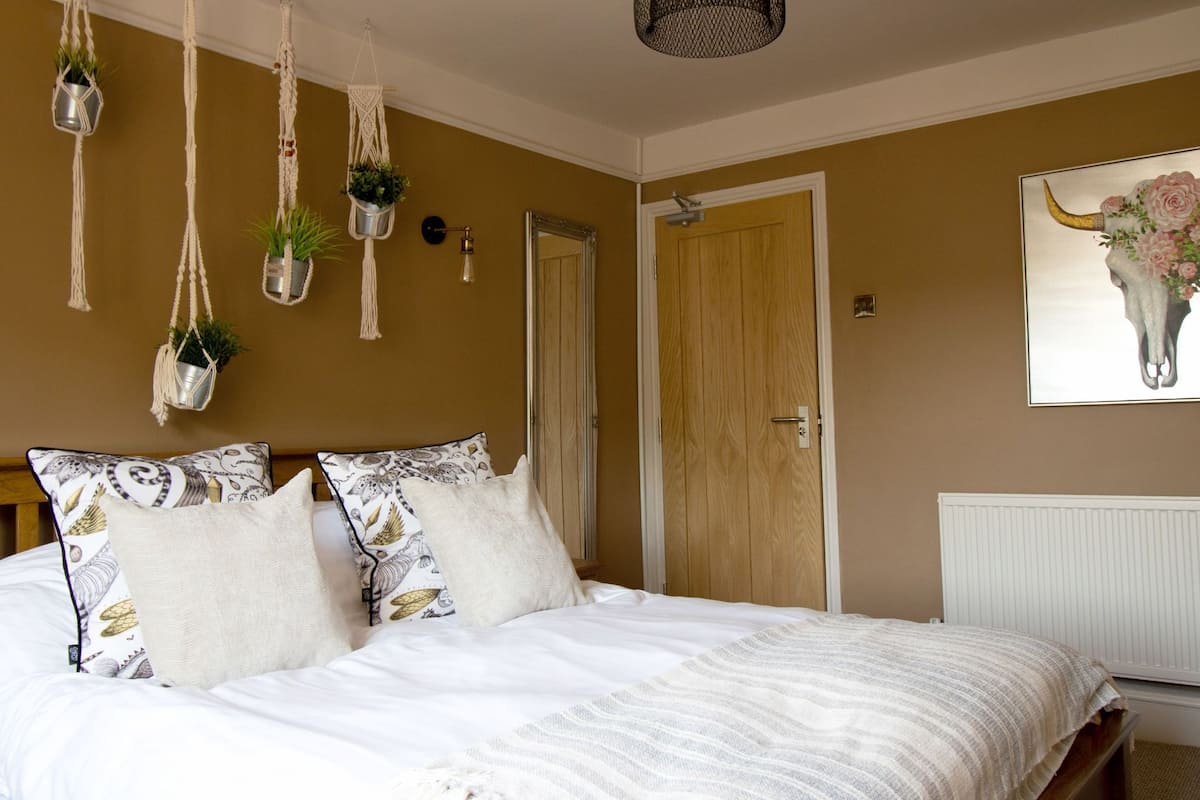 A bedroom with a bed, hanging macramé planters, a wooden door, and a wall-mounted artwork of a bull's head.