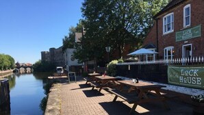 A riverside dining area with picnic tables and a brick pathway. - The Riverside Rooms (Newark)