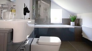 A modern bathroom with a bathtub, a toilet, and a sink. - The Riverside Rooms (Newark)