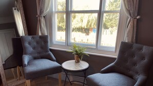 Two grey upholstered armchairs facing each other with a small round table and a potted plant between them. - The Riverside Rooms (Newark)