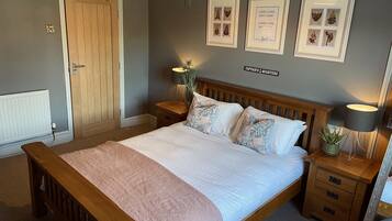 A bedroom with a wooden bed, two bedside tables, a nightstand, a potted plant, and framed artwork on the wall.