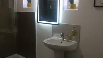 Un bagno con box doccia in vetro, un lavandino bianco con specchio e una finestra con piante.