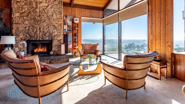 A modern living room with a stone fireplace, leather chairs, and a large window offering a city view. - Voted "Best Jet Liner Views" in LA Dogs Ok (Los Angeles)