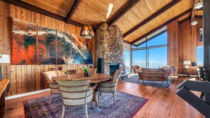A spacious room with wooden walls, a large painting, a stone fireplace, and a view of the ocean. - Voted "Best Jet Liner Views" in LA Dogs Ok (Los Angeles)