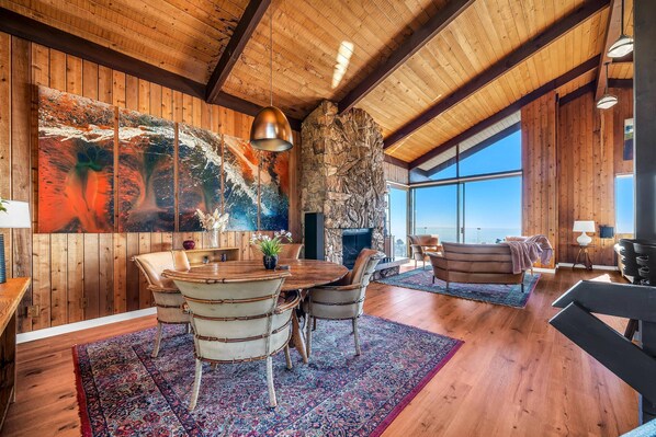 A spacious room with wooden walls, a large painting, a stone fireplace, and a view of the ocean.