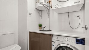 A modern bathroom with a built-in washing machine, a sink, and a shower. - Ebbtide 38 - On The Beach! (Forster)