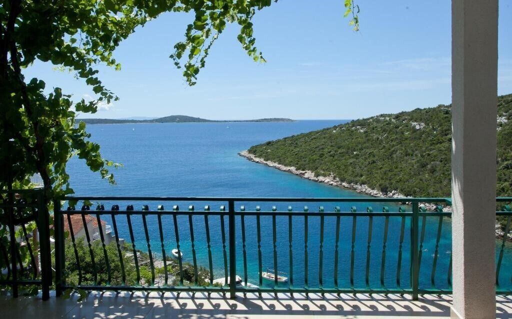 A balcony with a view of a turquoise sea and a rocky coastline.