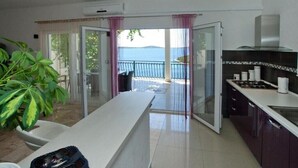Une cuisine moderne avec vue sur la mer, un balcon avec une porte vitrée et un coin repas agrémenté d’une plante.