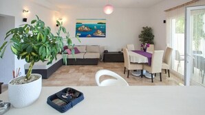 Un salon moderne avec un canapé, une table à manger et des chaises. On y trouve une grande plante en pot et un tableau accroché au mur.