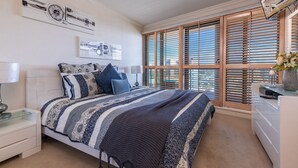 Un dormitorio con cama, mesitas de noche, cómoda y ventana con persianas.